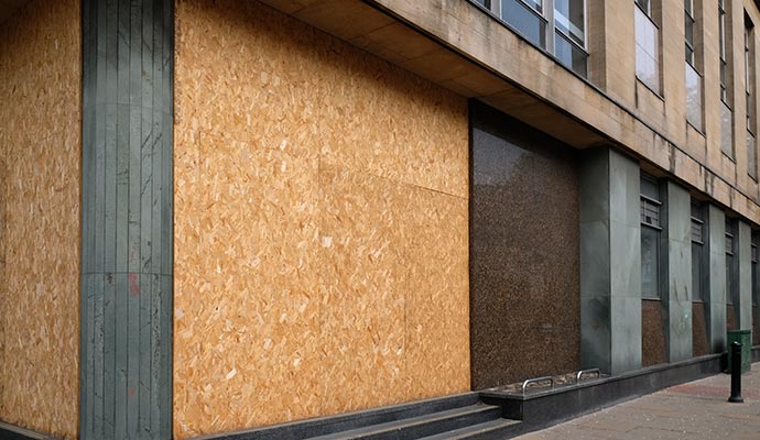 A building with windows and doors covered by wooden boards