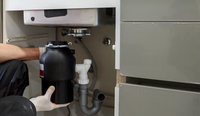 A person installing a garbage disposal unit under a kitchen sink